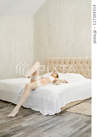 A woman in white underwear and stockings lies on the bed A woman in white underwear and stockings lies on the bed 117304314