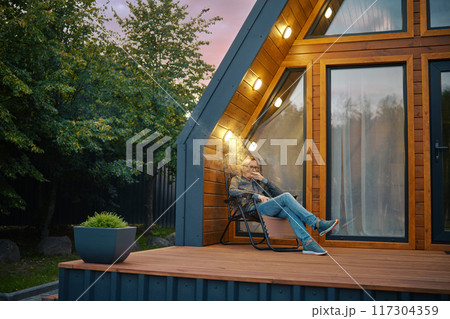 A man enjoys a cigar while sitting on the terrace of log cabin in the evening A man enjoys a cigar while sitting on the terrace of log cabin in the evening 117304359