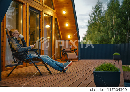 Man sipping tea in the evening and reading message from smartphone on the terrace 117304360