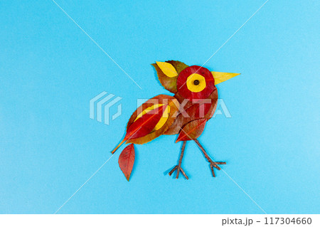 Creative depiction of bird made from colorful leaves against solid blue background. Intricately arranged leaves form birds body, wings, tail, and eye. use of natural elements captures essence bird 117304660