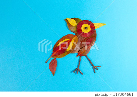 a bird made from various colorful autumn dry leaves against a solid blue background. natural elements, 117304661