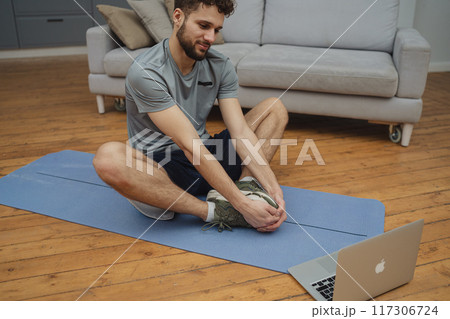 Training to become the best. Beautiful young man in sports clothing exercising at home. 117306724