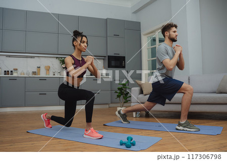 Training to become the best. Beautiful young woman and man in sports clothing exercising at home. 117306798