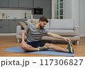 Training to become the best. Beautiful young man in sports clothing exercising at home. 117306827