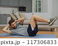 Training to become the best. Beautiful young man in sports clothing exercising at home. 117306833