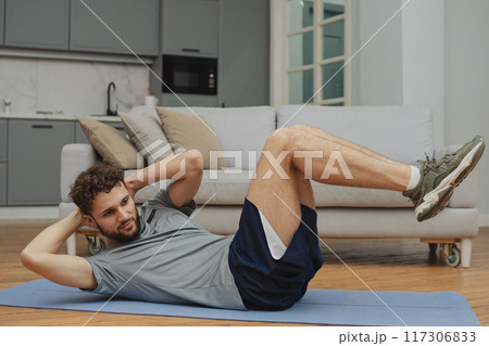 Training to become the best. Beautiful young man in sports clothing exercising at home. 117306833