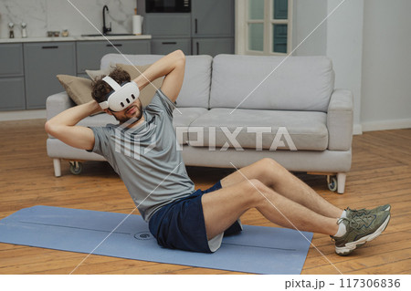 Training to become the best. Beautiful young man in sports clothing exercising at home. 117306836