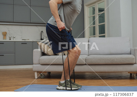 Training to become the best. Beautiful young man in sports clothing exercising at home. 117306837