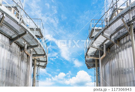 Two large metal tanks in a production facility surrounded by pipes 117306943