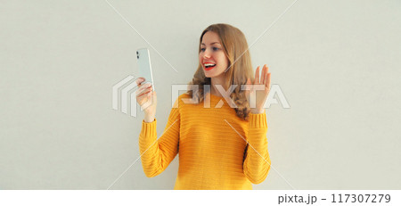 Happy smiling young woman taking selfie with phone or talking on video call waving hand on white 117307279