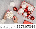 Red and white Christmas baubles in a box flat lay. Merry Christmas and Happy New Year seasons greetings card. Copy space. Festive full frame. Hands holding hot dink cup 117307344