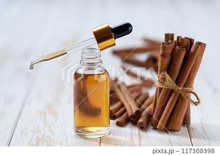 Cinnamon essential oil in a small bottle and cinnamon sticks on a white wooden table.Selective focus. Cinnamon essential oil in a small bottle and cinnamon sticks on a white wooden table.Selective focus. 117308398
