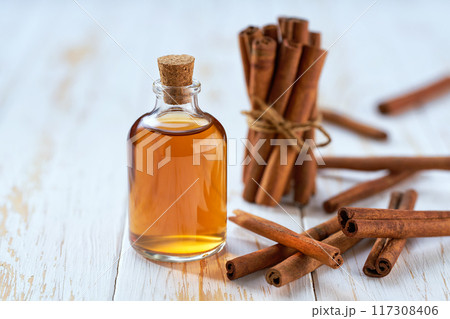 A bottle of essential cinnamon oil with cinnamon sticks on a white wooden table. 117308406