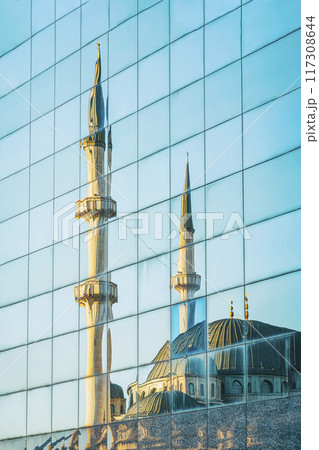 A mosque with minarets is reflected in the glass facade of modern building A mosque with minarets is reflected in the glass facade of modern building 117308644