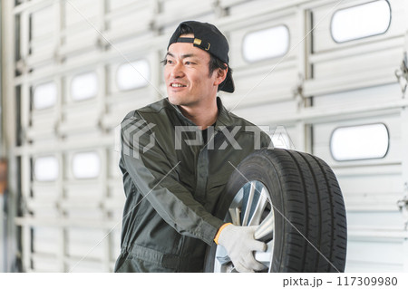 タイヤを持って挨拶する自動車整備士・メカニックの中年アジア人男性 117309980