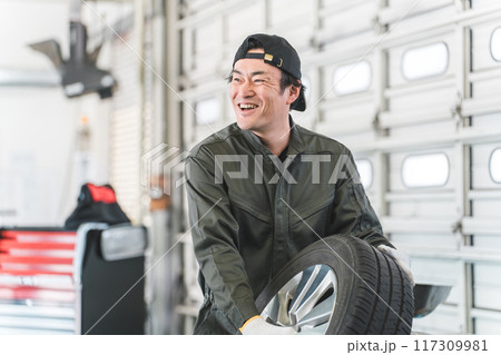 タイヤを持って挨拶する自動車整備士・メカニックの中年アジア人男性 117309981
