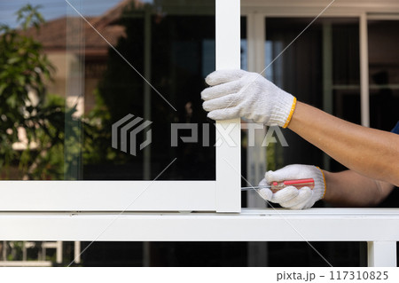 Handyman repairing the sliding window. Adjust a rail wheel and lock hook. 117310825