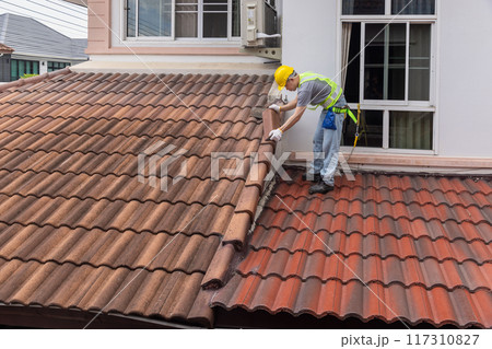 Worker fixing eaves and tiles of the old roof. 117310827