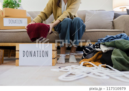 Young Asian women sit in living room sorting clothes for donation in a donation box second hand clothes. Donate concept 117310979