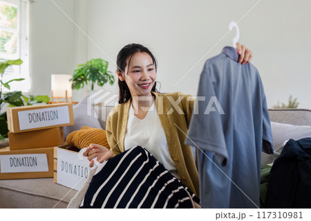 Young Asian women sit in living room sorting clothes for donation in a donation box second hand clothes. Donate concept 117310981