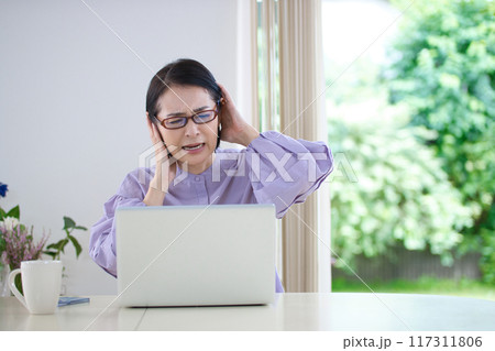 リビングでパソコンを見ながら頭を抱えるミドル女性 117311806
