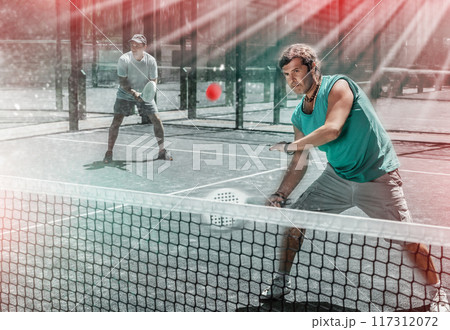 Men play padel on an outdoor tennis court. Hitting the ball with racket 117312072