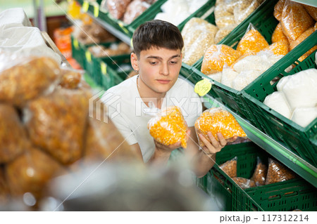 Thinking guy stands in department of supermarket and chooses packaged products Thinking guy stands in department of supermarket and chooses packaged products 117312214
