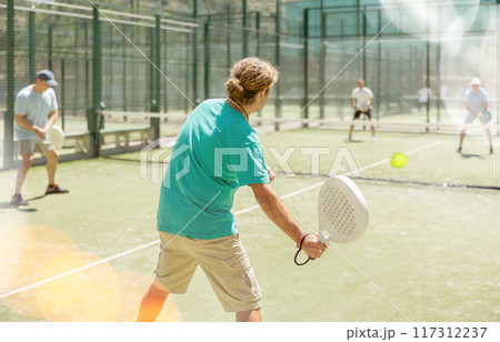 Men play padel on an outdoor tennis court. Hitting the ball with racket 117312237