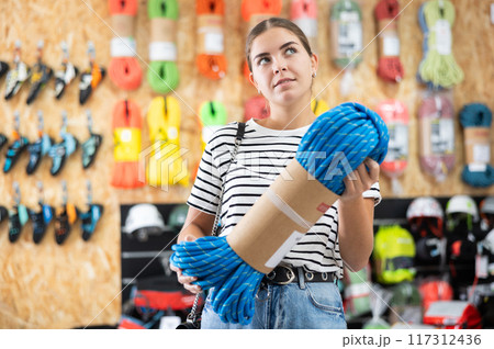 Young girl chooses and buys climbing rope for trip to the mountains in sports equipment store 117312436