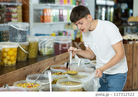 Guy scooping pickled olives in the produce section of supermarket Guy scooping pickled olives in the produce section of supermarket 117312522
