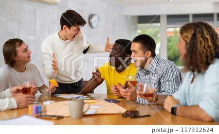 Group of enthusiastic men playing board game sitting around table Group of enthusiastic men playing board game sitting around table 117312624