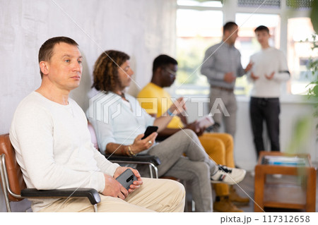 Middle-aged male visitor sitting on chair in waiting hall of clinic 117312658