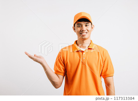 Portrait Asian smiling young delivery man showing something with empty open palm hands studio isolated white background, Happy lifestyle men carry person in an orange shirt uniform 117313384