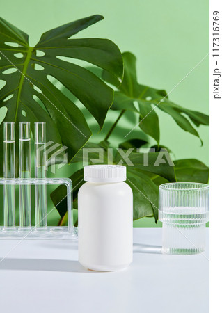 On the white and green table background, an unbranded medicine box is displayed along with a glass of water and test tubes. Front view, scene for medicinal product advertising On the white and green table background, an unbranded medicine box is displayed along with a glass of water and test tubes. Front view, scene for medicinal product advertising 117316769