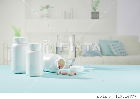 The blue table on the living room floor holds unlabeled medicine bottles and glass cups of water. Blank medicine bottle labels for design and advertising 117316777