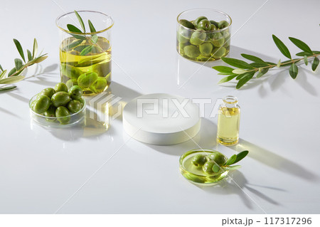 On the white background, beaker and petri dishes filled with olives, olives oil and leaves decorated. A white empty podium for display product with ingredient from olive On the white background, beaker and petri dishes filled with olives, olives oil and leaves decorated. A white empty podium for display product with ingredient from olive 117317296
