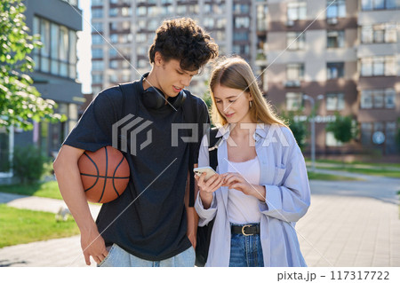 Young teenage guy and girl walking, looking at smartphone together, urban background Young teenage guy and girl walking, looking at smartphone together, urban background 117317722
