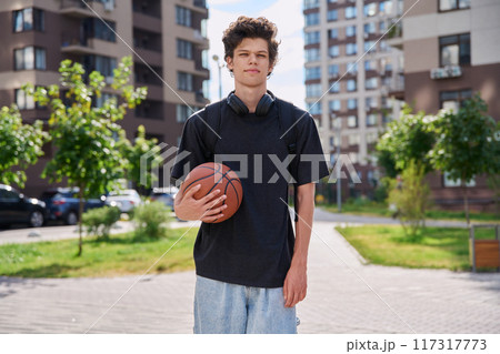 Young male with backpack basketball ball looking at camera outdoors, modern city Young male with backpack basketball ball looking at camera outdoors, modern city 117317773