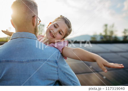 Father with girl on roof with solar panels, hugging. Rooftop solar or photovoltaic system. Sustainable future for next generation. 117319040