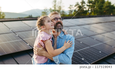 Father with girl on roof with solar panels, hugging, looking at the sky. Rooftop solar or photovoltaic system. Sustainable future for next generation. Father with girl on roof with solar panels, hugging, looking at the sky. Rooftop solar or photovoltaic system. Sustainable future for next generation. 117319043