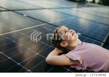 Cute girl lying on solar panels roof, shot with copy space. Rooftop solar or photovoltaic system. Sustainable future for next generation. 117319046