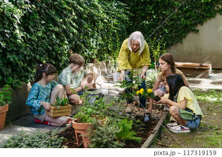 Students and female teacher at outdoor sustainable education class. Kids taking care of plants in school garden. Concept of experiential learning and ecoliteracy. 117319159