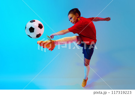 Dynamic photo of female soccer player in action kicks ball in neon light against colorful gradient background. 117319223