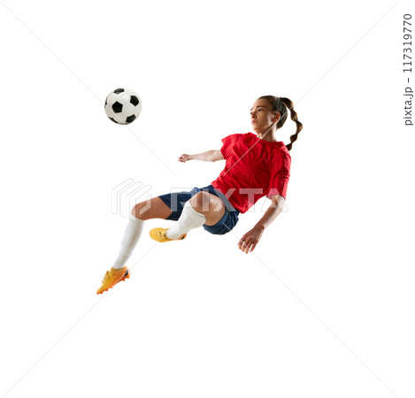 Mid-flight female soccer player, hair flying, as she powerfully kicks ball in acrobatic move against white studio background. 117319770