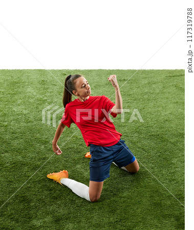 Female football player kneeling on green grass at stadium in triumphant pose and clenching fists, shouting of joy. Score winning goal in final game. Female football player kneeling on green grass at stadium in triumphant pose and clenching fists, shouting of joy. Score winning goal in final game. 117319788