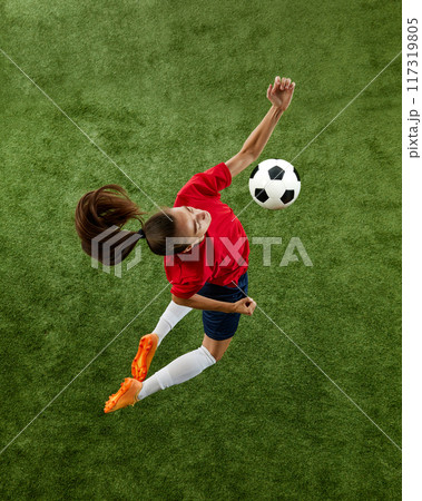 Aerial view of young athletic woman, football defender wearing comfortable uniform hitting ball with chest in mid air. Aerial view of young athletic woman, football defender wearing comfortable uniform hitting ball with chest in mid air. 117319805