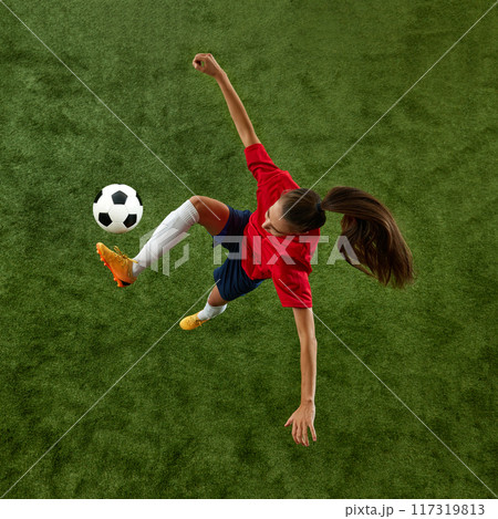 Top view image of young sporty woman, soccer athlete doing exercises for balance and attentiveness on green lush stadium. Top view image of young sporty woman, soccer athlete doing exercises for balance and attentiveness on green lush stadium. 117319813
