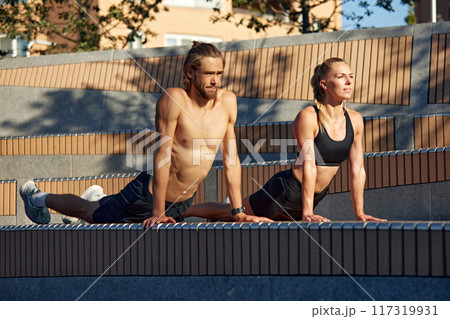 Sportive young people, man and woman training outdoors, doing stretching, Pilates, yoga exercises in early summer morning 117319931