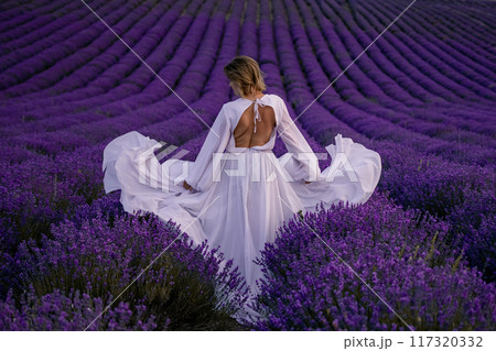 A woman in a white dress is standing in a field of purple flowers 117320332