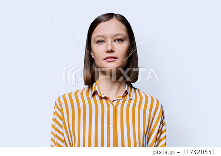 Portrait of young serious woman looking at camera on white background Portrait of young serious woman looking at camera on white background 117320551